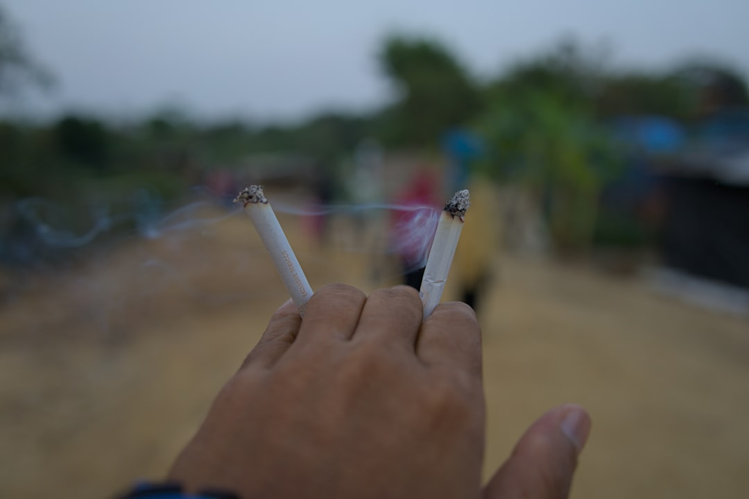 Hand holds two lit cigarettes with smoke.
