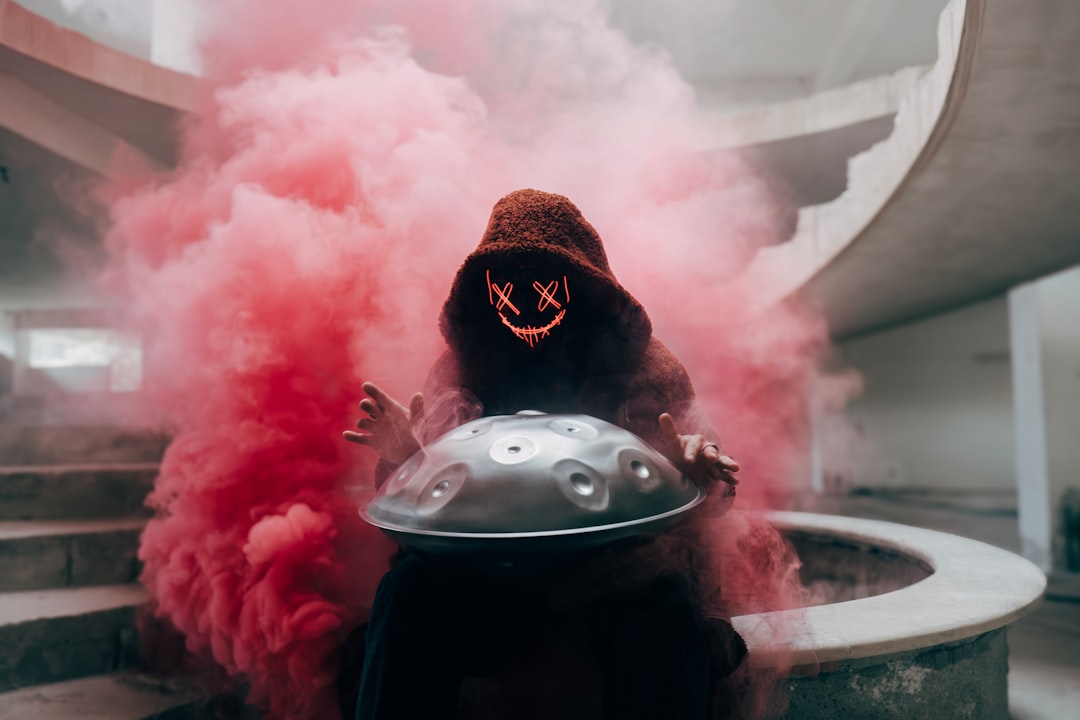 a person wearing a hood and holding a helmet in front of a cloud of smoke