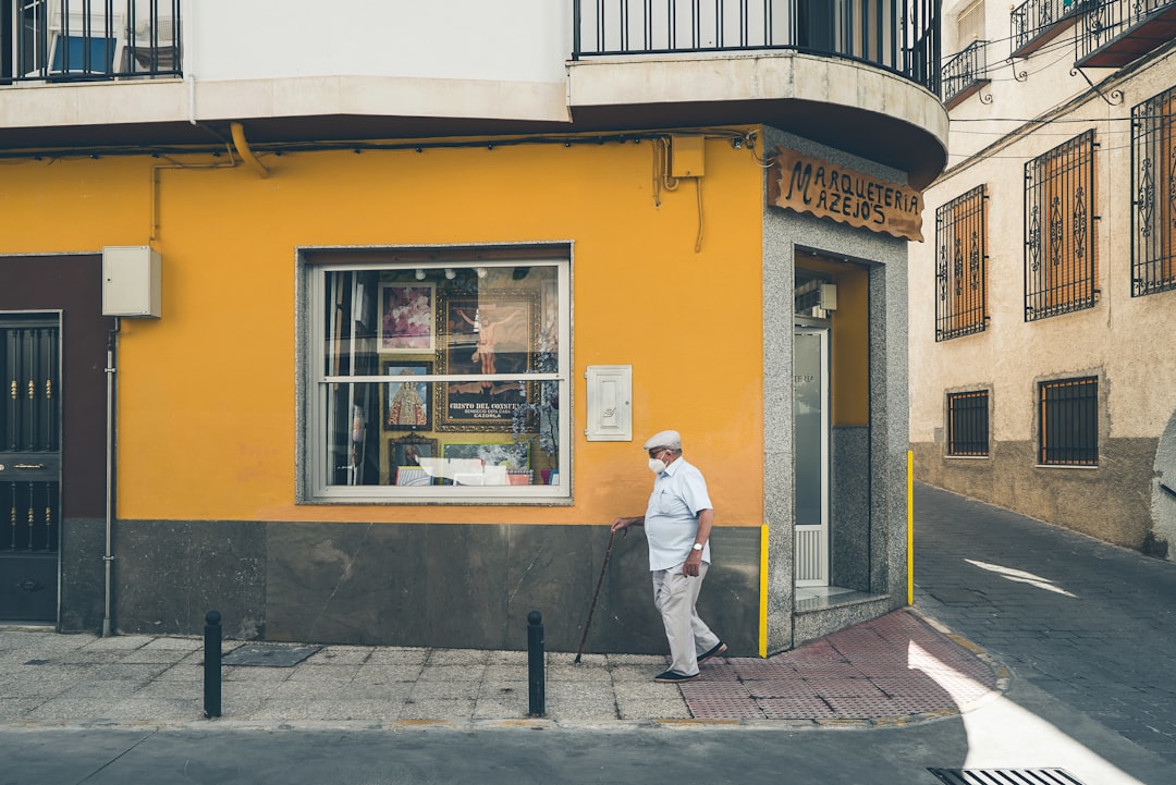 man in white dress shirt and blue denim jeans standing in front of yellow painted building